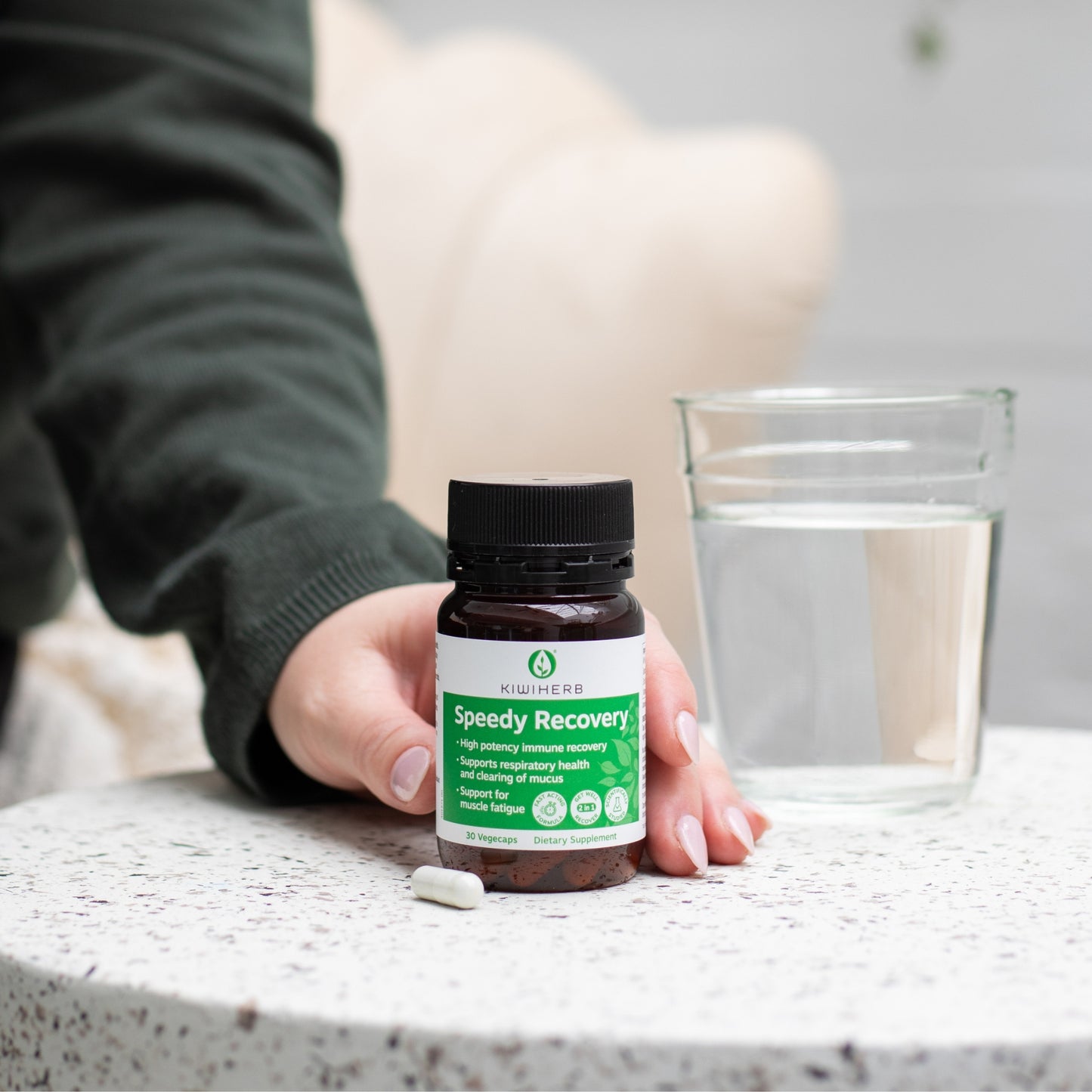 A woman holding a bottle of Kiwiherb Speedy Recovery with a glass of water.