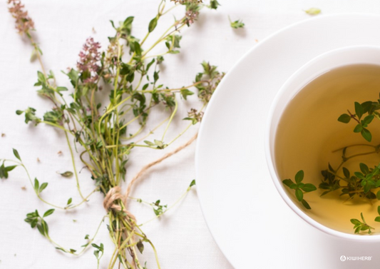 cup of thyme tea in a white cup with thyme branches in the tea and on the table