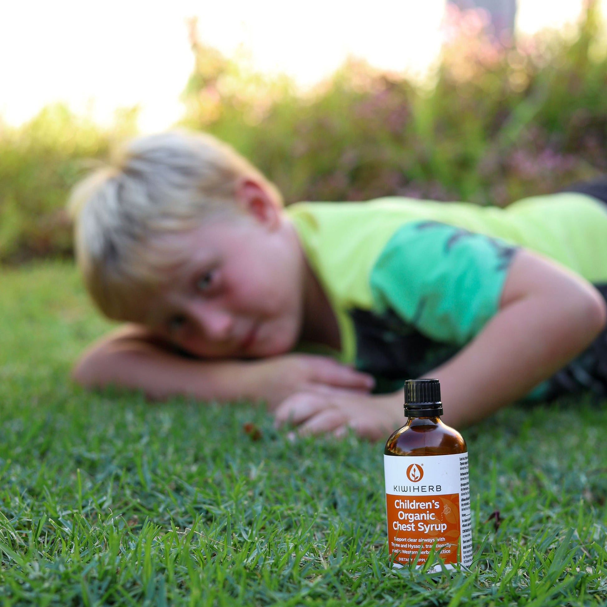 Child lying on grass with a bottle of children's organic Chest Syrup in the foreground.