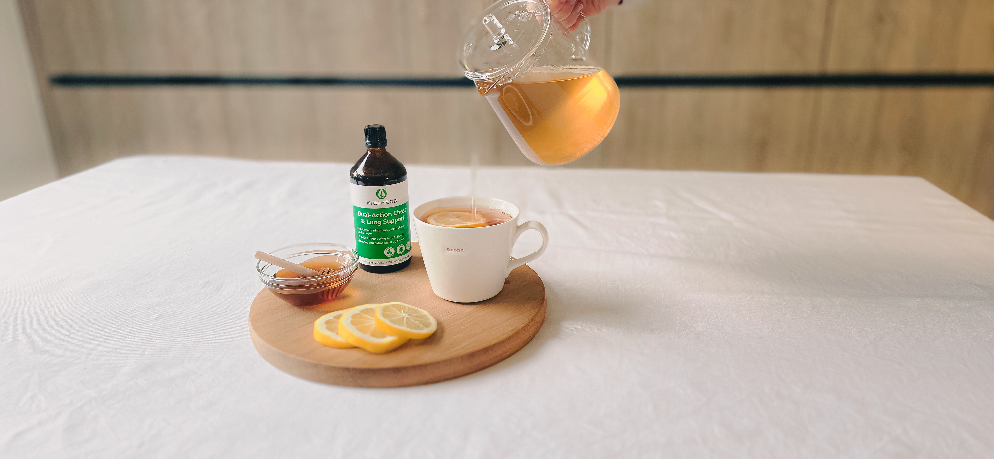 Tea being poured into a cup with a bottle and lemon slices on a wooden board.