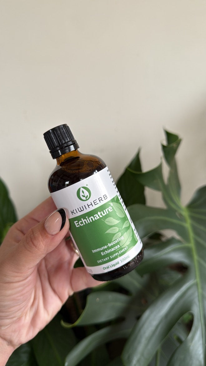 Hand holding a bottle of Echinature with a plant in the background