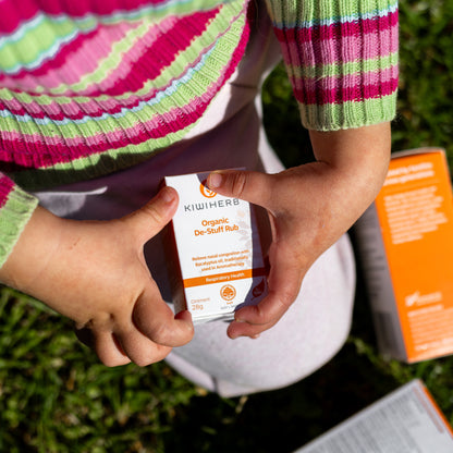 Child holding Kiwiherb Organic De-Stuff Rub, a BioGro certified herbal balm for clearing blocked noses naturally in babies and toddlers.