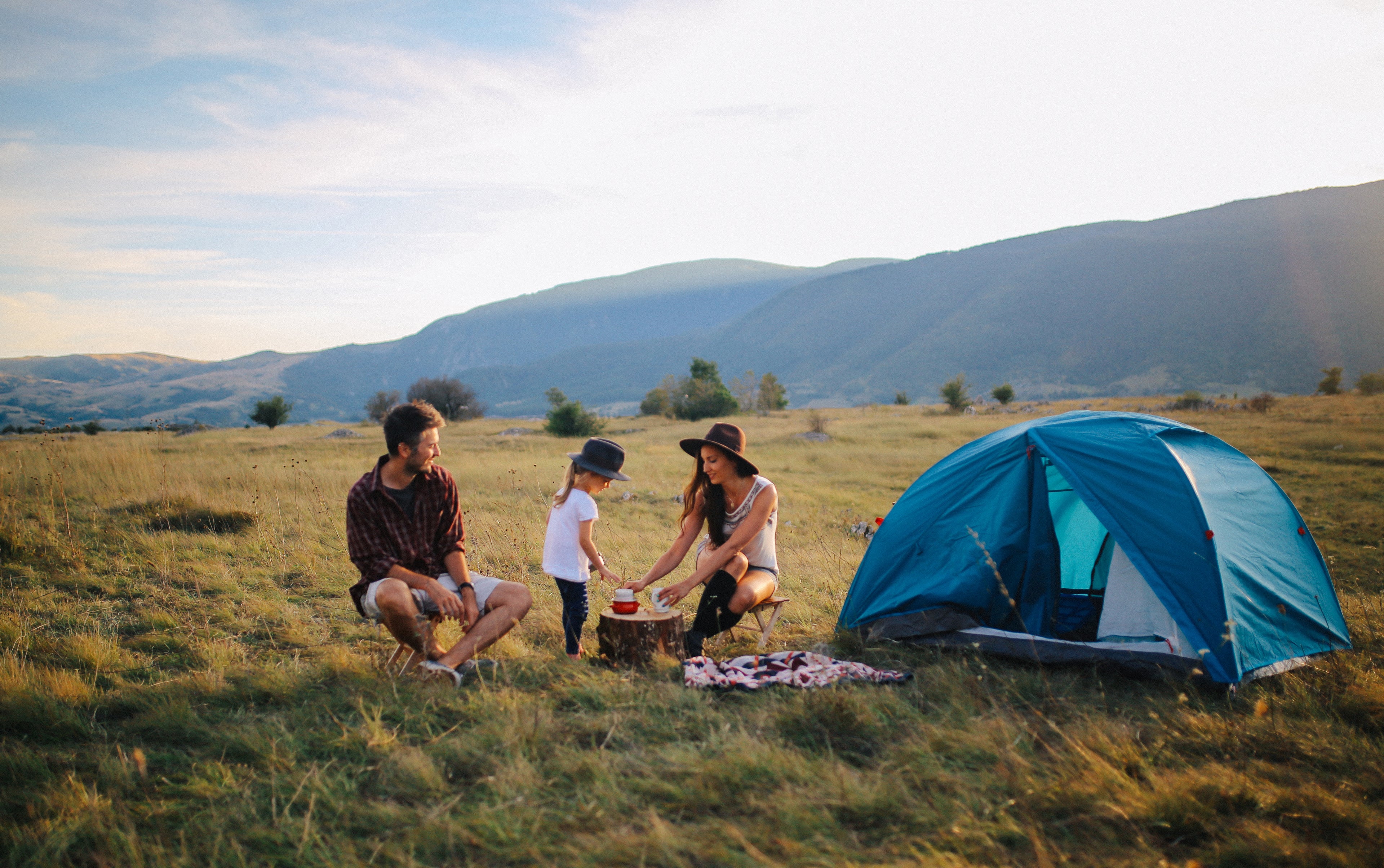 Young father, mother and daughter camping in a tundra below large hills.